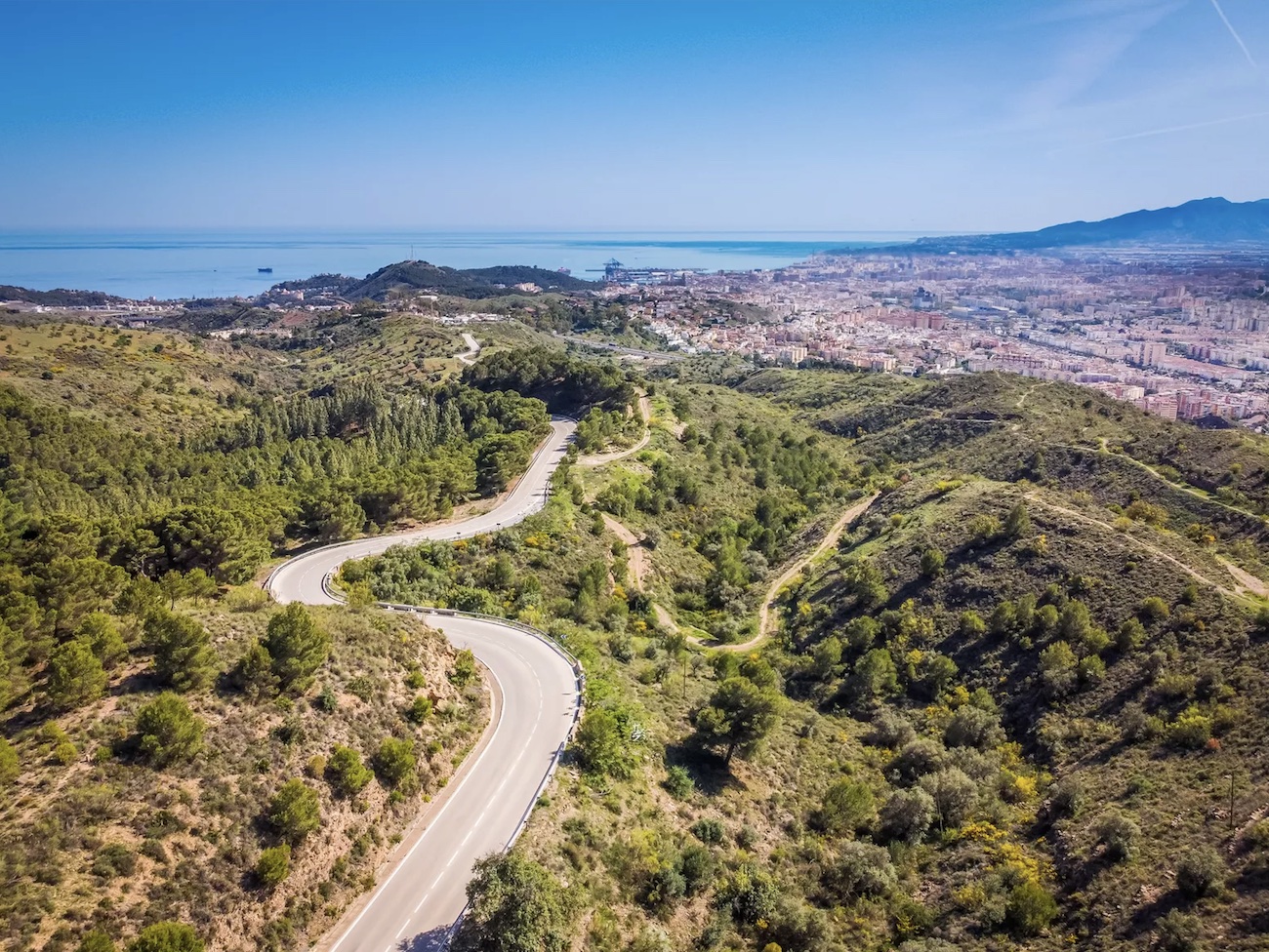 Panoramic view of Malaga with majestic mountains, cityscape, and sea, ideal for spring hiking adventures.