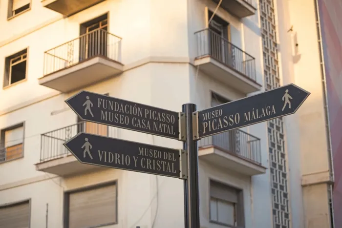 Directional signage to Picasso Museum, Malaga, with other museum pointers against a backdrop of historic city architecture.